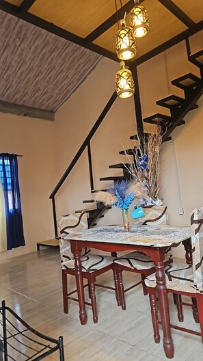 Ein Essbereich mit einem Holztisch und Stühlen, einer Vase mit Trockenpflanzen und einer Treppe im Hintergrund.