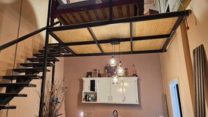 A staircase with a wooden finish and metal railings, leading to a white cabinet area with hanging lights. - Charming 1-bedroom Loft apartment with AC in Herstelling Demerara. (Herstelling)