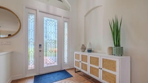 A hallway with a white door, a blue doormat, a white cabinet with woven doors, and a green plant. - Moondance Villa (Cape Coral)