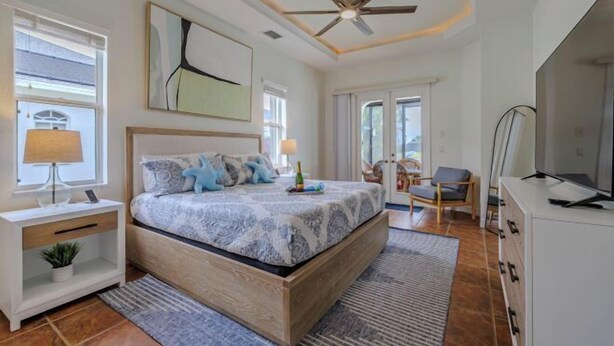 A bedroom with a bed, bedside tables, a ceiling fan, and a large window. - Moondance Villa (Cape Coral)