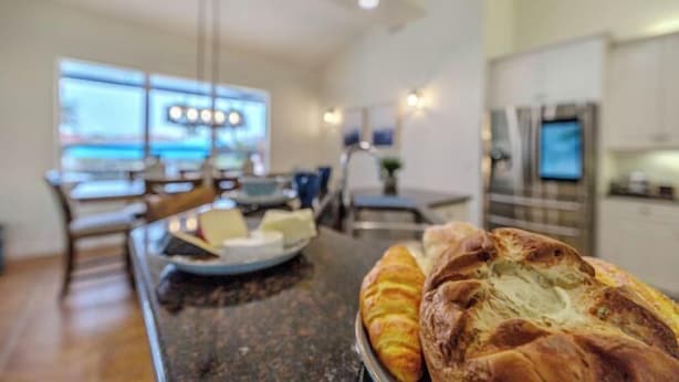 A modern kitchen with a marble countertop, a large window, and a dining area with wooden chairs. - Moondance Villa (Cape Coral)