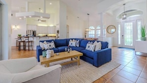 A spacious living room with a blue sofa, a wooden coffee table, and a ceiling fan. - Moondance Villa (Cape Coral)