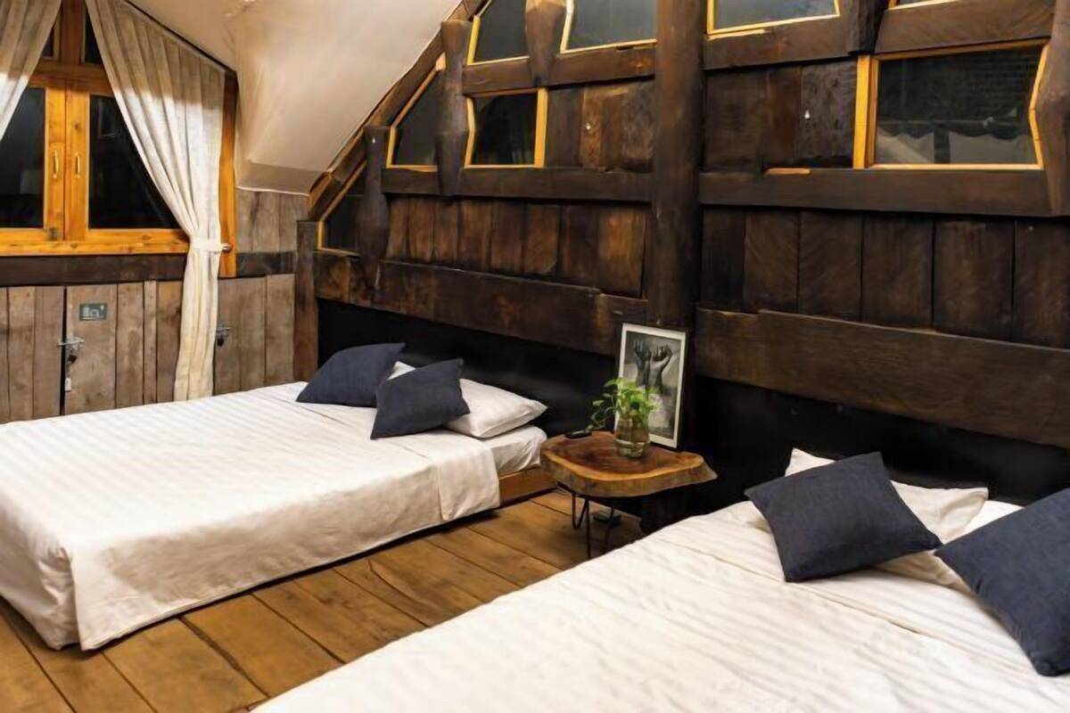Een slaapkamer met twee bedden, houten wanden, een klein houten tafeltje en een raam met gordijnen.