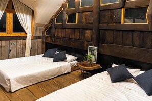 Een slaapkamer met twee bedden, houten wanden, een klein houten tafeltje en een raam met gordijnen.