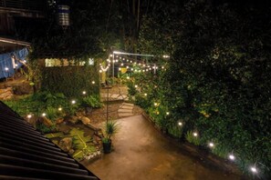 Ein beleuchteter Gartenpfad bei Nacht, mit Lichterketten und Blumentöpfen.