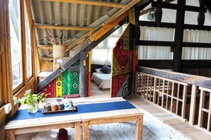 Een rustiek houten cabin interieur met een wenteltrap, een eethoek met een tafel en stoelen, en een kleurrijke muurschildering.