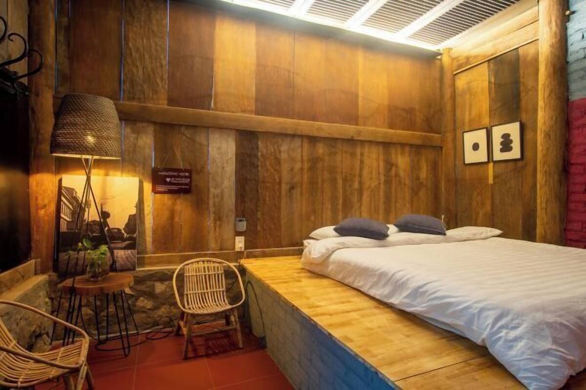 Een houten kamer met een bed, een stoel, een lamp en een kleine tafel.