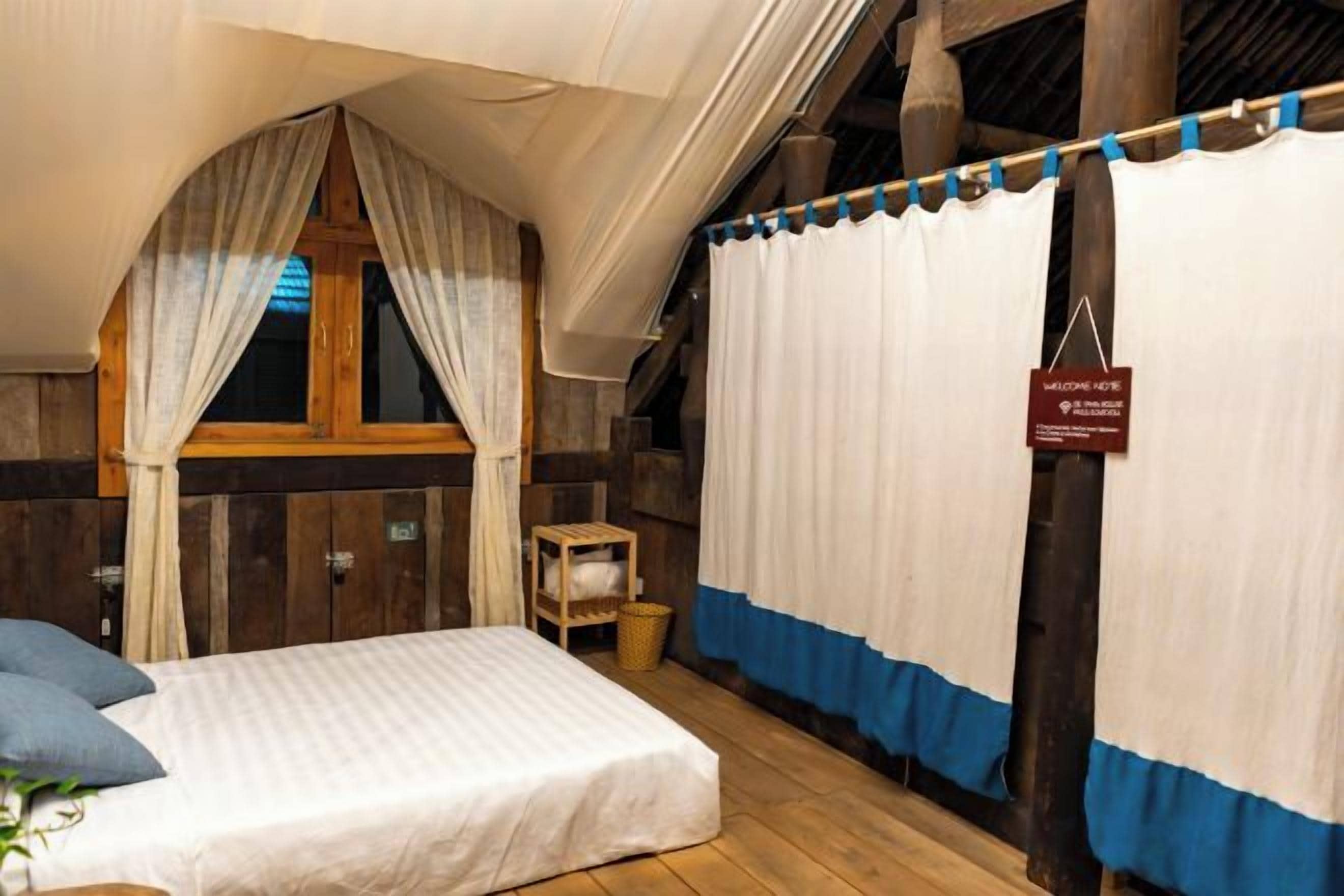 A bedroom with a bed, a window with curtains, a wooden wall, and a sign.