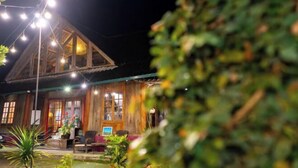 Un bâtiment rustique en bois, doté d’un toit en pente, de guirlandes lumineuses et d’un petit espace extérieur aménagé avec une table et des chaises.