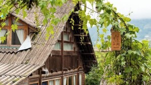 Une maison traditionnelle en bois, dotée d’un toit à pente, entourée de verdure et avec une chaîne de montagnes en toile de fond.