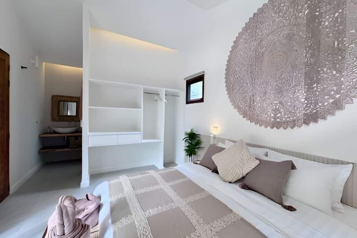 A bedroom with a bed, a large decorative wall piece, a bedside table, and a nightstand.