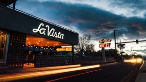 A motel named La Vista with a neon sign, a visible entrance, and a street view with cars passing by. - Midnight Cactus Room | La Vista Motel | 203 (Denver)