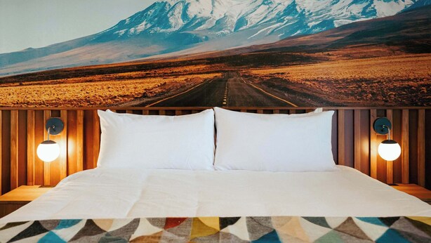 Una cama con sábanas blancas, dos almohadas y un plaid estampado con motivos geométricos.