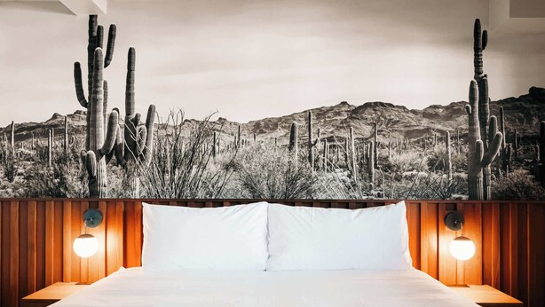 Ein Hotelzimmer mit einem Bett, weißen Kissen und einer großen Wandmalerei im Wüstendesign.