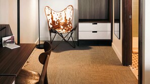 Ein modernes Hotelzimmer mit einem Holztisch, einem Ledersessel, einer Couch, einem Bett, einem Kleiderschrank, einem Spiegel und einem Bild an der Wand.