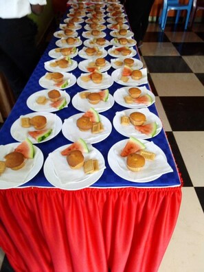 A long table with multiple plates of food, each containing a muffin and a slice of watermelon.