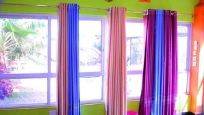 A room with a large window, curtains in various colors, and a view of palm trees outside. - kuwetu resort and conference (Muthara)