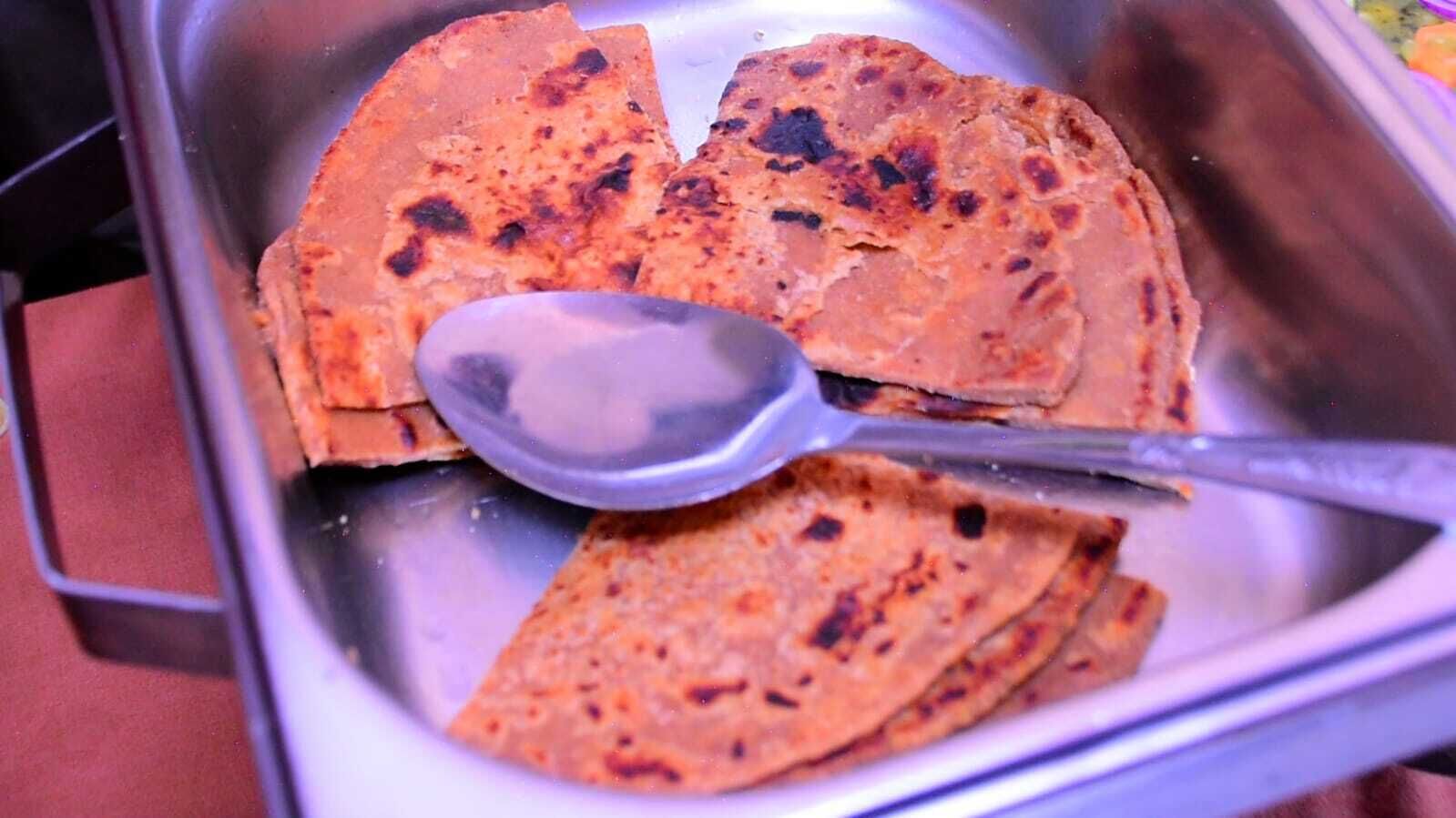 A metal container with a spoon, containing flatbreads with charred spots.