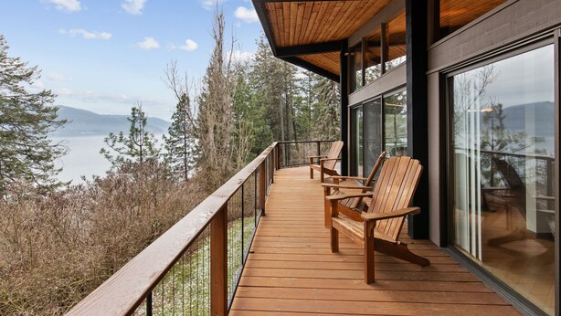 Une terrasse en bois avec des chaises, donnant sur un lac et une forêt.