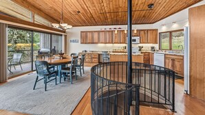 Une cuisine moderne avec des meubles en bois, un coin repas doté d’une table ronde et une grande fenêtre donnant sur un jardin.