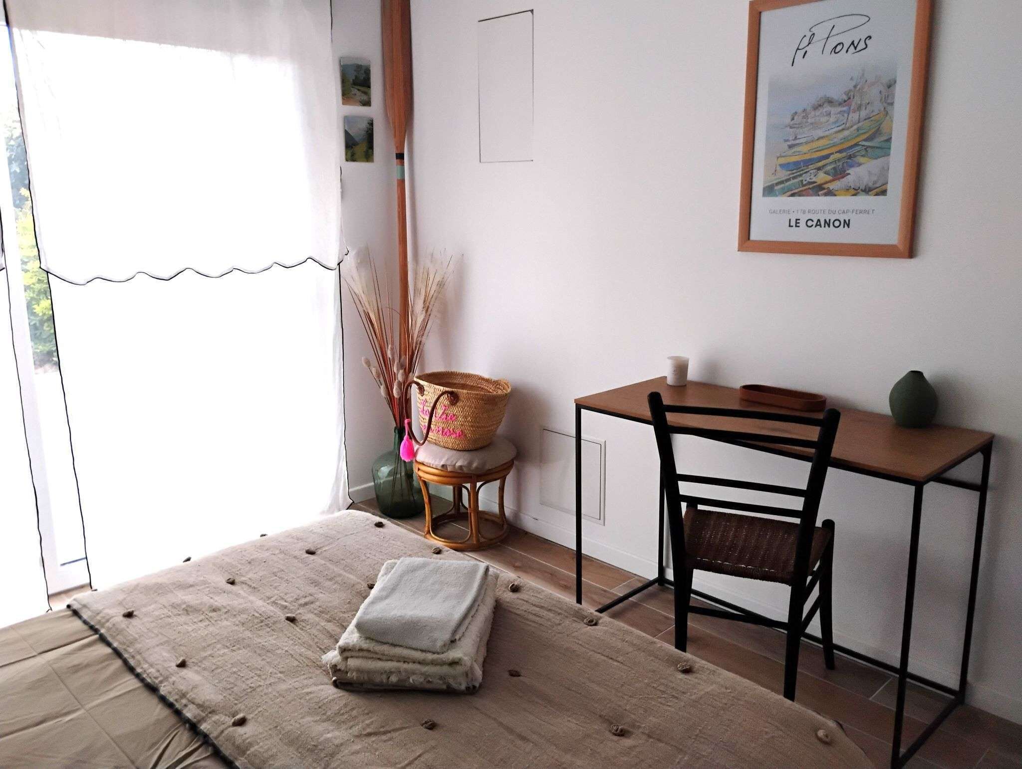 A cozy room with a bed, a small wooden desk, a chair, and a framed picture on the wall.