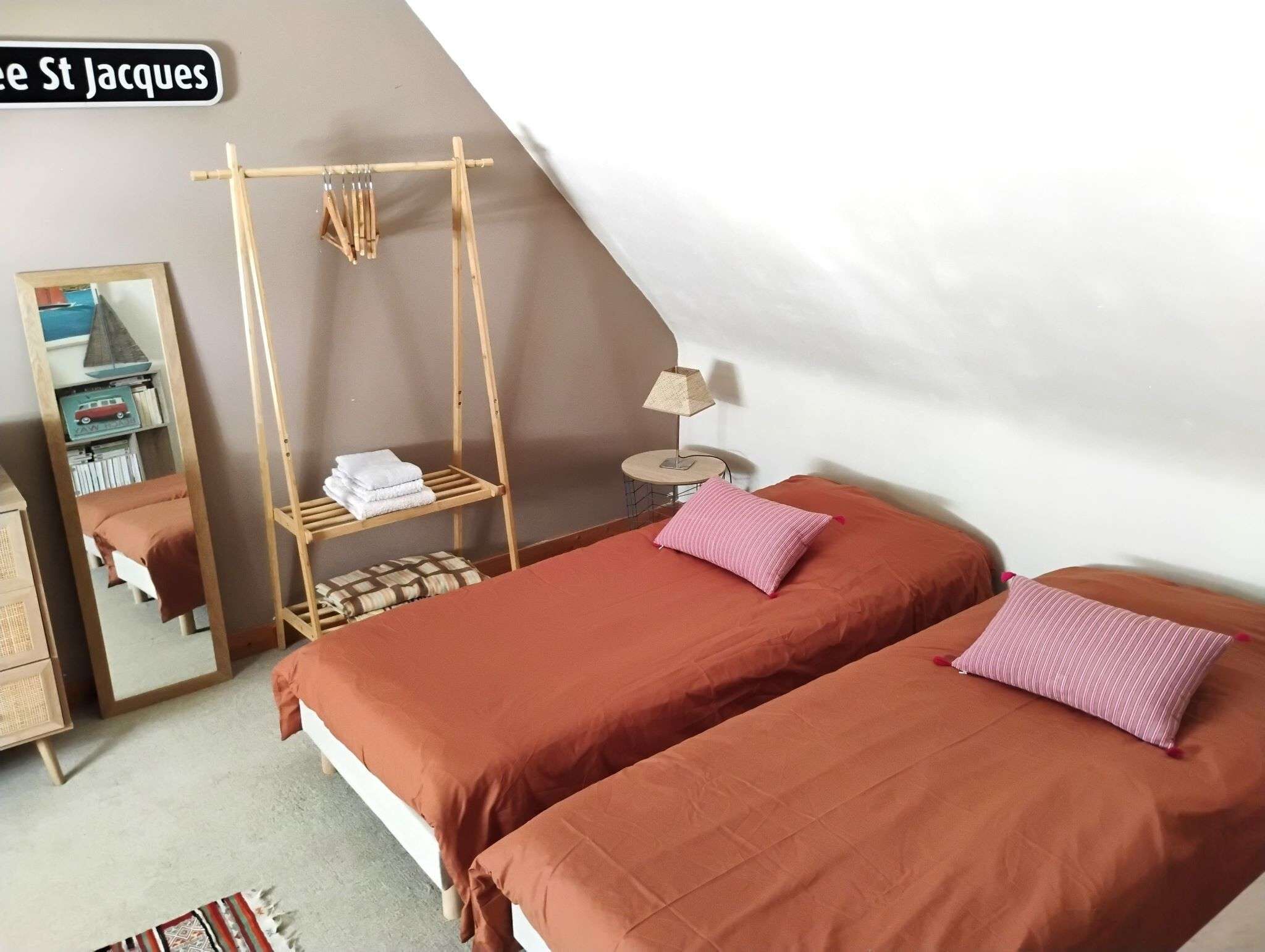 Een slaapkamer met twee bedden, een houten rek, een spiegel, een lamp en een plank met boeken en een speelgoed.