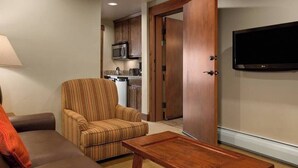 A living room with a sofa, a striped armchair, a wooden coffee table, a television, and a kitchen area visible through an open door. - Quaint 3-bedroom condo in Breckenridge perfect for your getaway (Breckenridge)
