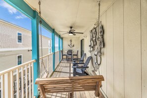 A covered outdoor area with a ceiling fan, wooden bench, and chairs, overlooking a building with a window. - Beachfront Retreat! Pool, Balcony & Family Loft (Gulf Shores)