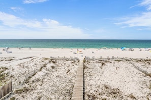Ein Strand mit einer Holzpromenade, die zum Wasser führt, Sanddünen und Strandsonnenschirmen.