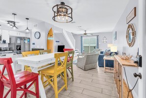 A modern kitchen with white cabinets, a dining area with colorful chairs, a staircase, and a living room with a sofa and a coffee table. - Beachfront Retreat! Pool, Balcony & Family Loft (Gulf Shores)