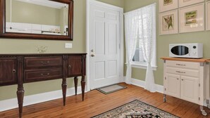 A room with a wooden floor, a white door, a mirror, a microwave, and a patterned rug. - Newly Renovated Victorian APT, Steps from Forsyth Park (Savannah)