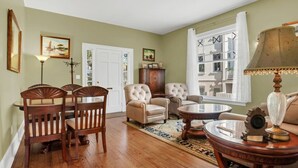 A living room with a dining area, a fireplace, and a large window with curtains. - Newly Renovated Victorian APT, Steps from Forsyth Park (Savannah)