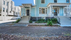 A row of light blue townhouses with a central staircase leading to the entrance, a small garden area, and a paved walkway. - Newly Renovated Victorian APT, Steps from Forsyth Park (Savannah)