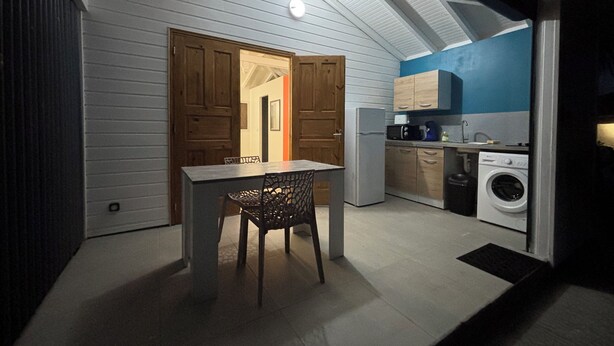 Une cuisine compacte équipée d’un lave-linge, d’une table avec des chaises et de meubles de rangement en bois.