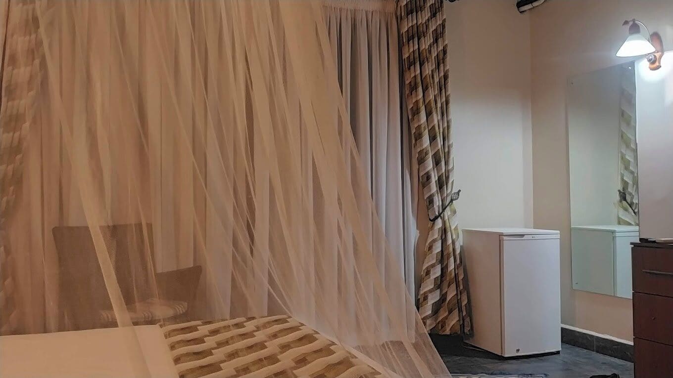 A bedroom with a bed, a bedside table, a small white appliance, and a mirror on the wall.