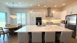 Una cocina moderna con una isla grande, armarios blancos, electrodomésticos de acero inoxidable e iluminación colgante.