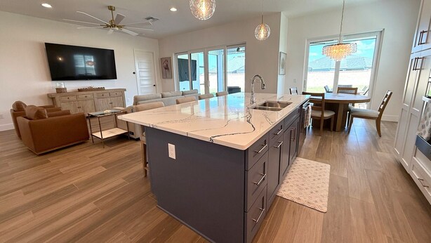 Una cocina moderna con una isla grande, un comedor con candelabro y una sala de estar con televisor.
