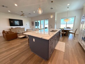 Una cocina moderna con una isla grande, un comedor con candelabro y una sala de estar con televisor.