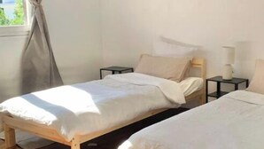 A room with two wooden beds, a window with curtains, a bedside table with a lamp, and a wooden floor. - Charming house with terrace near Paris (Viry-Châtillon)