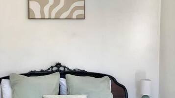 Un dormitorio con cama, almohadas, una mesita de noche y una obra de arte en la pared.