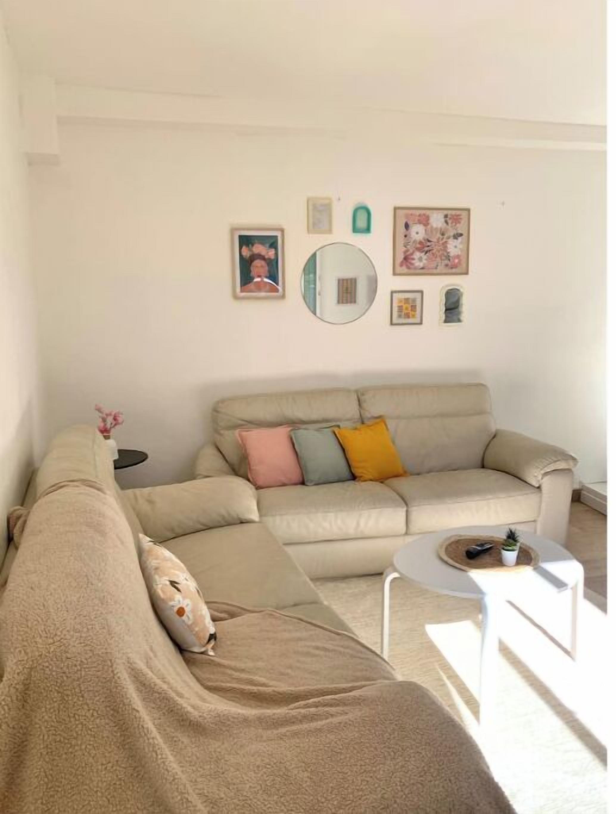 Un salon avec un canapé beige, un miroir rond et une petite table blanche.