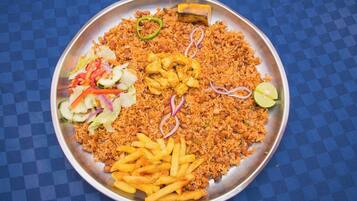 Un plato grande de metal con diversos alimentos, como arroz, pollo y papas fritas, acompañado de una ensalada y gajos de limón.