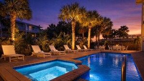 A poolside area with lounge chairs, a pool, and palm trees.