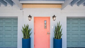 A building with a pink door, two potted plants, and two garage doors.