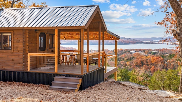 Une cabane en bois dotée d’une terrasse et d’un espace salon extérieur, offrant une vue imprenable sur une vallée et un lac pittoresques.