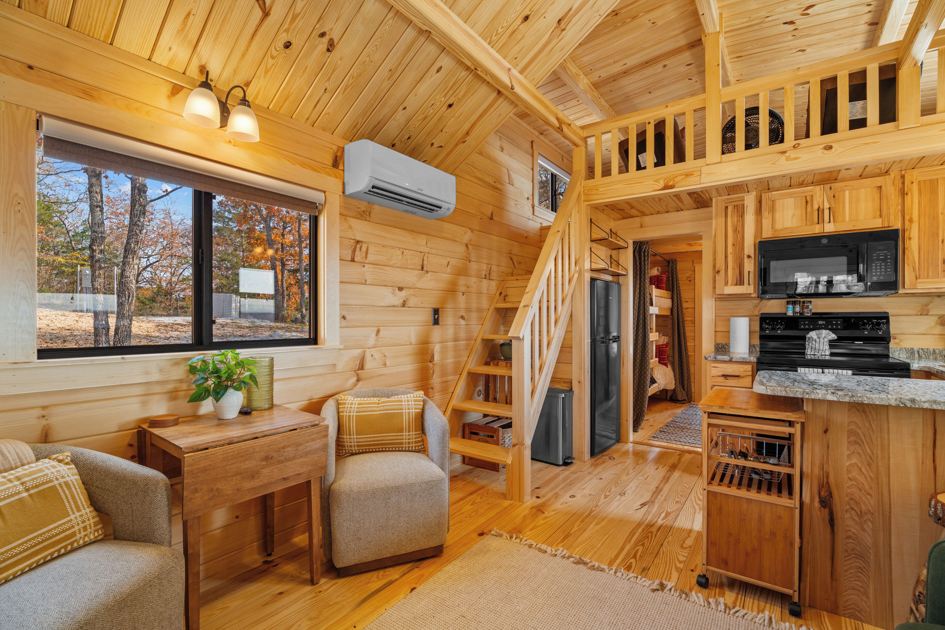 A cabin interior with wooden walls, a kitchen area, a dining space, and a staircase.