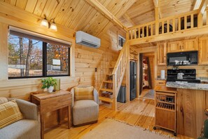 A cabin interior with wooden walls, a kitchen area, a dining space, and a staircase. - Tucked Away Tiny Home Retreat | Sleeps 6 | Incredible Views (Reeds Spring)
