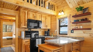 Une cuisine rustique, située dans une cabane en bois, avec un plan de travail en granit, des placards en bois, un four à micro-ondes, une cuisinière et un évier.