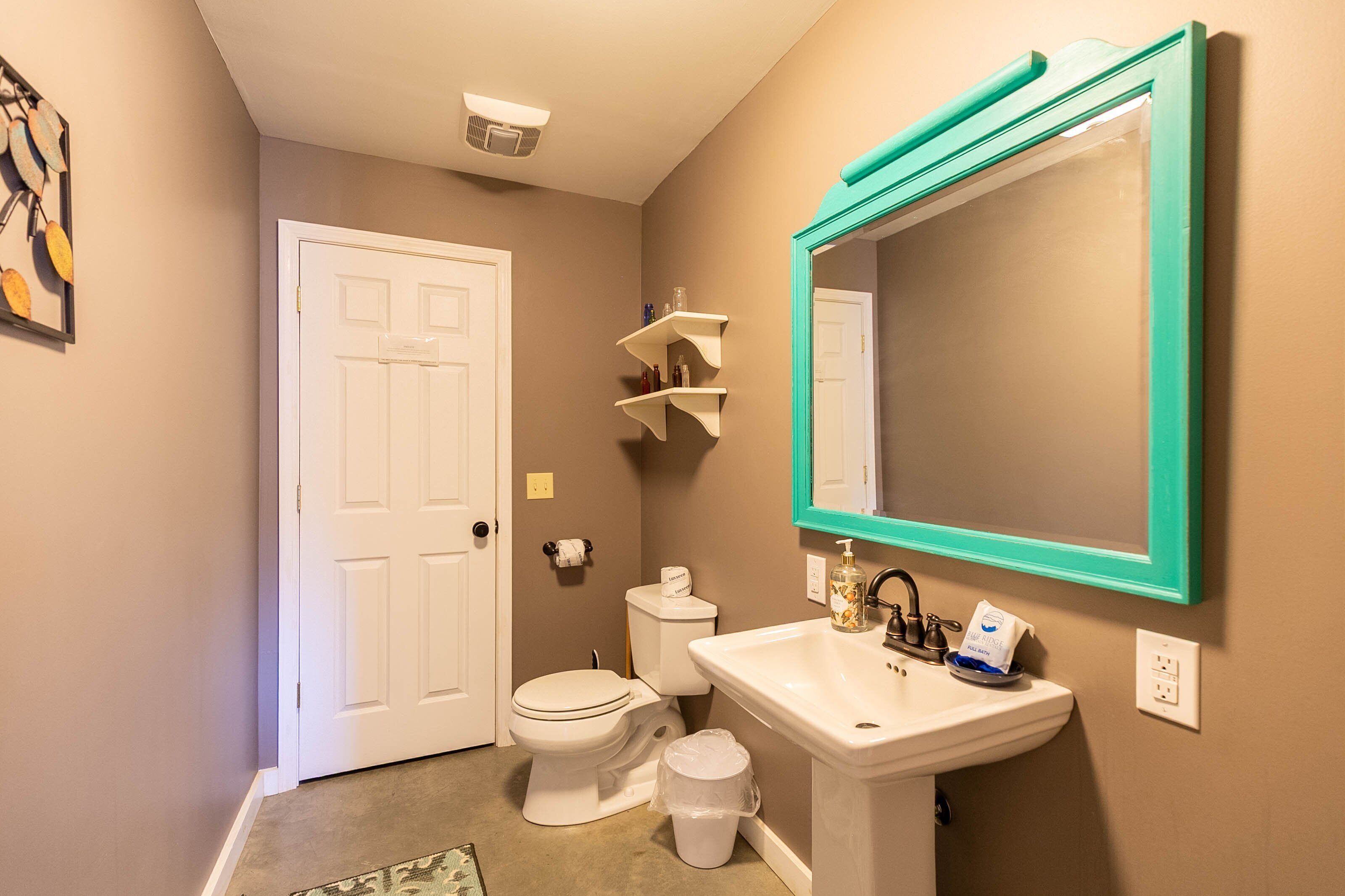 A bathroom with a white toilet, a sink with a teal-framed mirror, and a beige wall.