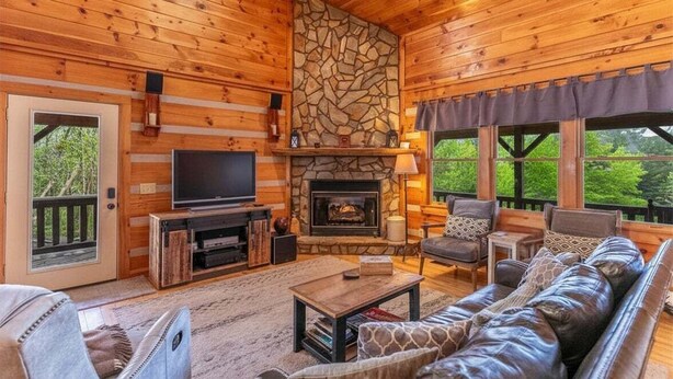 L'intérieur d'une cabane en rondins, avec une cheminée en pierre, un téléviseur et un canapé.